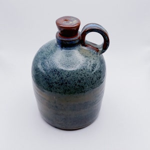 May include: A blue and brown ceramic jug with a speckled glaze and a brown lid. The jug has a handle and a rounded body.