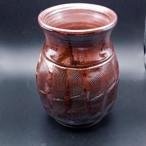 May include: A brown ceramic vase with a wavy pattern. The vase has a wide mouth and a rounded body.