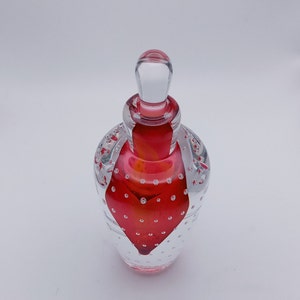 May include: A clear glass perfume bottle with a red heart-shaped design. The bottle has a clear stopper and is decorated with small air bubbles throughout the glass. The red color is vibrant and eye-catching.