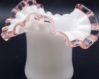 May include: A white glass vase with a ruffled pink rim. The vase is a classic design with a simple, elegant shape.