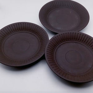 May include: Three brown paper plates with a fluted edge. The plates are arranged in a triangular shape on a white surface.