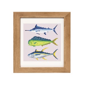 May include: A framed cross-stitch artwork featuring three different types of fish: a marlin, a mahi-mahi, and a tuna. The fish are depicted in a colorful, pixelated style against a light pink background.