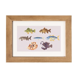 Puede incluir: Un bordado de punto de cruz enmarcado con varios peces en estilo pixelado. Los peces son en tonos de verde, marrón, azul y amarillo, con un rape morado oscuro. El marco es de madera marrón claro y el fondo es rosa claro.