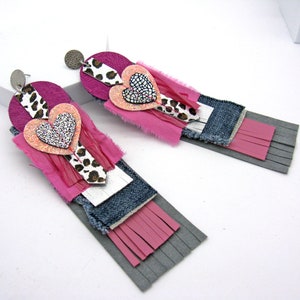 Könnte beinhalten: Ein Paar lange, rosa und graue Ohrringe mit einem mehrschichtigen Design. Die Ohrringe haben ein pinkfarbenes Herz mit Glitzer, einen Stoff mit Leopardenmuster und einen Jeansstoff.