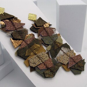 Puede incluir: Pendientes abstractos con un cuadrado dorado y una cascada de formas. Los pendientes presentan una mezcla de texturas y colores, incluyendo marrón, cobre y oro. El diseño incorpora elementos texturizados y brillantes.