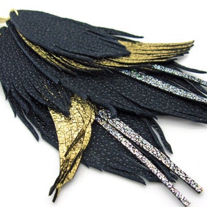 May include: Black leather earrings with gold and silver detailing. The earrings feature layered, fringed black leather, with gold and silver metallic leather accents. The earrings have a gold-coloured hook.