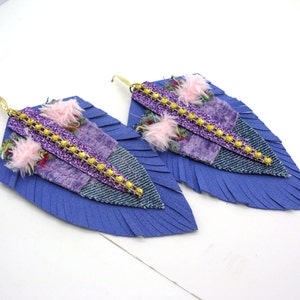 Könnte beinhalten: Ein Paar violette und blaue Federn-Ohrringe mit goldenen Kettenakzenten und rosa flauschigen Verzierungen.