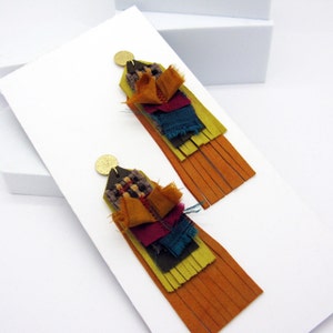 May include: A pair of long, colorful tassel earrings with a layered fabric design. The earrings are made with a variety of fabrics in shades of green, yellow, orange, red, and blue. The tassels are made of a soft, suede-like material.
