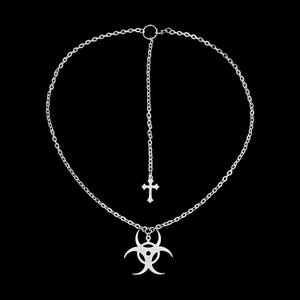 Op de afbeelding: Zilverkleurige ketting met een kettingontwerp, een kruisvormige hanger en een hanger met een biohazard-symbool. De ketting heeft een Y-vormige druppel met een klein kruis. De achtergrond is zwart.