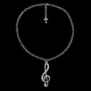 Puede incluir: Un collar plateado con un colgante de clave de sol y un pequeño dije de cruz. La cadena es delicada y el collar tiene un cierre de mosquetón. El fondo es negro, resaltando la joya.