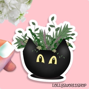May include: Black cat planter with green and purple plants growing out of the top. The planter has a white outline.