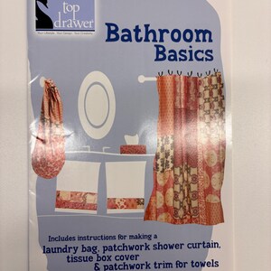 Può includere: Un libretto di istruzioni azzurro intitolato Bathroom Basics di top drawer. La copertina presenta illustrazioni di un sacco per la biancheria, una tenda da doccia patchwork, un copriscatola per fazzoletti e asciugamani con bordo patchwork.