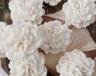 May include: Seven white, flower-shaped candles arranged on a white surface. The candles are made to look like carnations.