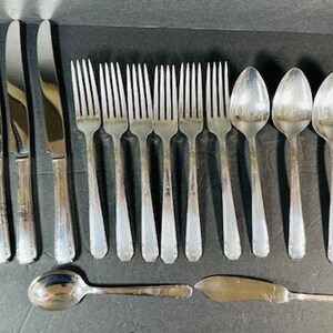 Puede incluir: Un juego de cubiertos de plata pulida, que incluye cuchillos, tenedores y cucharas. Los cubiertos están dispuestos en filas sobre una superficie oscura.