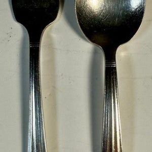 May include: A silver fork and spoon. The fork has four prongs, and the spoon has a rounded bowl. Both items have decorative handles with a floral design. The set is made of a shiny, reflective metal.