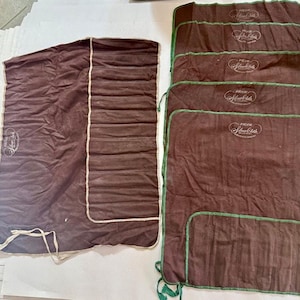 May include: A collection of brown Pacific Silvercloth storage bags. The bags have a rectangular shape with green trim and the Pacific Silvercloth logo. One bag is rolled up, and the others are folded flat.