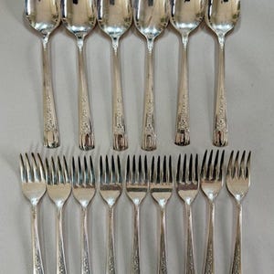 May include: A set of 10 silver forks and 10 silver spoons. The forks and spoons have ornate designs and are arranged in two rows.