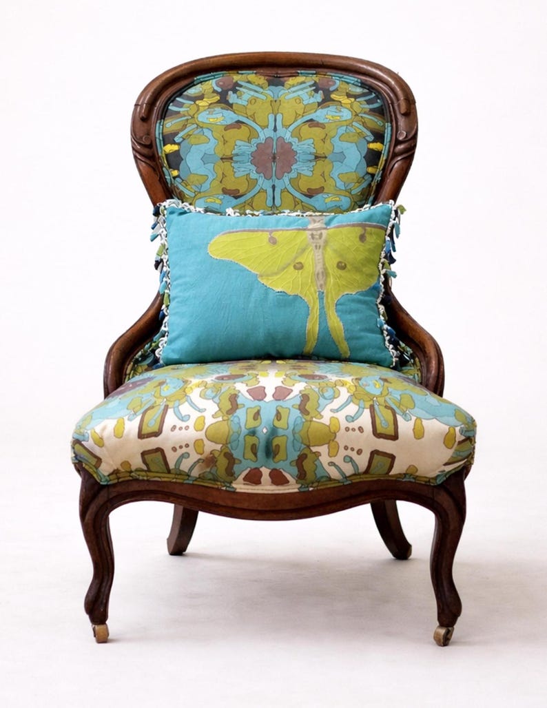 Pu&ograve; includere: Sedia antica in legno con seduta e schienale fantasia, e un cuscino turchese con un disegno di falena gialla. La sedia ha gambe curve e uno schienale decorativo, creando un'estetica vintage.