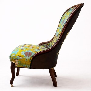 Pu&ograve; includere: Sedia antica con schienale alto e struttura in legno curvata. La seduta e lo schienale sono rivestiti con un colorato motivo floreale nei toni del giallo, blu e rosso. La sedia ha quattro gambe curve.