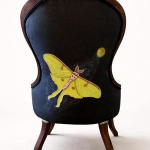 Pu&ograve; includere: Una piccola sedia in stile antico con schienale imbottito nero. Sullo schienale &egrave; dipinta una grande falena gialla con ali dettagliate, insieme a una luna gialla e una scia di punti bianchi. La sedia ha gambe e struttura in legno scuro.