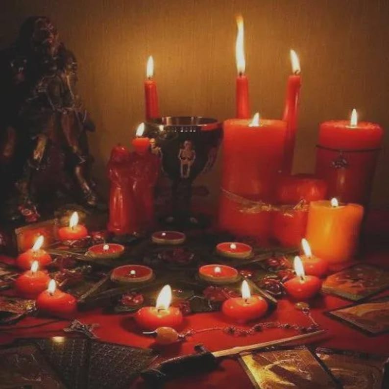Pu&ograve; includere: Una collezione di candele rosse accese di varie dimensioni, tra cui candele a colonna e votive, disposte su una superficie rossa. Un calice decorativo e una statua scura sono anch'essi presenti, creando un'atmosfera mistica. La scena &egrave; illuminata dal caldo bagliore delle fiamme.
