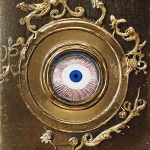 May include: An elaborate gold frame encases a central eye motif. The eye has a blue iris, white sclera, and pink-purple details. The frame is adorned with decorative flourishes with blue accents, set against a dark brown background.