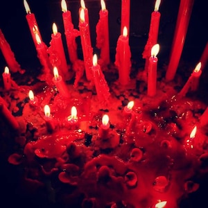 Peut inclure: Une collection de nombreuses bougies effilées rouges brûlant avec des flammes vives. Les bougies sont de hauteurs variées, avec de la cire rouge fondue épaisse qui s'accumule et coule pour former une base texturée et inégale.