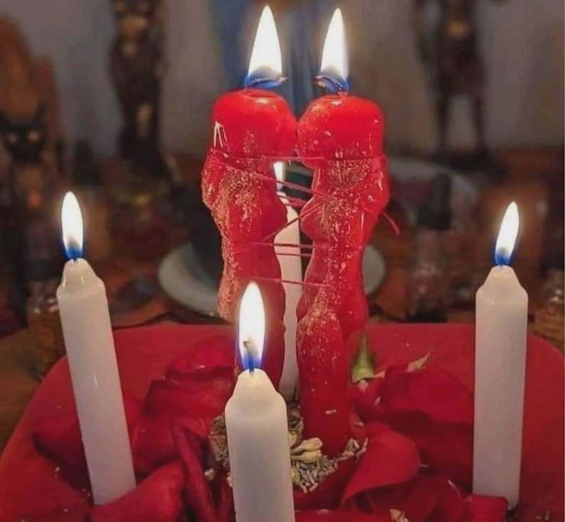 Pu&ograve; includere: Una collezione di candele accese, tra cui due grandi candele rosse legate con uno spago rosso. Sono accese anche tre candele bianche, con fiamme visibili. Le candele sono disposte su una superficie rossa con petali di rosa rossi.