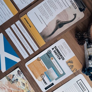 May include: A close-up of a brown clipboard with a yellow and white paper on it. The paper has the title "Loch Ness Monster" and a picture of the Loch Ness Monster. The paper also has text about the Loch Ness Monster. There is a map of Scotland on the table next to the clipboard.