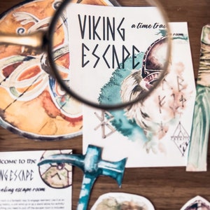Może przedstawiać: Zbliżenie gry escape room o tematyce wikingów. Gra zawiera karty z tekstem "VIKING ESCAPE" i "a time travel room". Karty zawierają akwarelowe ilustracje hełmu wikinga, run i młota.