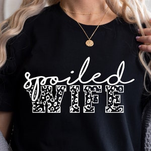 May include: Black t-shirt with the text "spoiled WIFE" in white with a leopard print pattern.