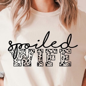 May include: White t-shirt with the text "spoiled WIFE" in black lettering. The letters are filled with a leopard print pattern.