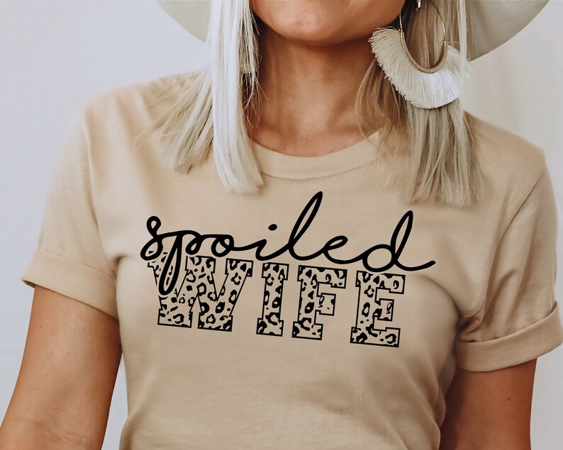 May include: A beige t-shirt with the text "spoiled WIFE" in black lettering. The letters are filled with a leopard print pattern.