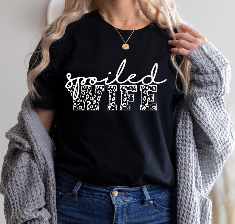 May include: Black t-shirt with the text "spoiled WIFE" in white with a leopard print pattern.