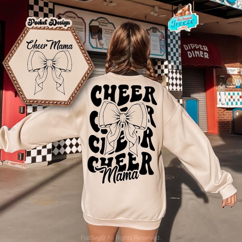May include: A cream-colored sweatshirt with a black graphic design that says "CHEER" with a large bow in the middle and "Mama" at the bottom. The graphic is in a retro style font.