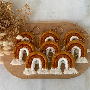 Pode incluir: Um conjunto de oito chaveiros arco-íris com franjas brancas. Cada chaveiro é feito de fio e tem um anel de metal dourado.