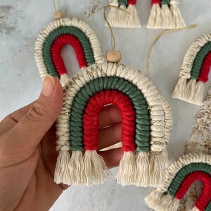 May include: A set of five handmade Christmas ornaments shaped like rainbows. Each ornament is made of yarn in red, green, and white with gold accents. The ornaments have a wooden bead at the top for hanging.