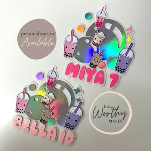 May include: Two personalised iridescent holographic stickers with a bubble tea theme. The stickers feature a large bubble tea cup with smaller bubble tea cups around it. The stickers also feature the names "Bella" and "Miya" in pink glitter letters.