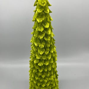 May include: A lime green, cone-shaped Christmas tree made of paper. The tree is decorated with a layered, scaly design.
