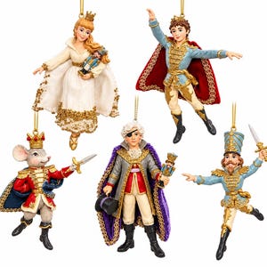 May include: A set of five Nutcracker-themed hanging ornaments featuring a princess in a white gown, a prince in a blue jacket with a red cape, a mouse in a red uniform, a figure in a gray coat with a purple cape, and a soldier in a blue uniform.