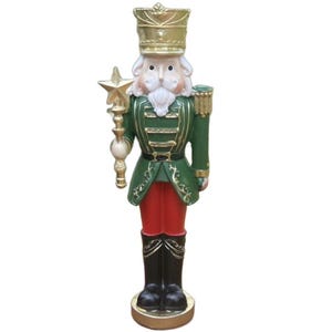 May include: A decorative Christmas nutcracker figurine. The figurine is dressed in a green jacket, red pants, and black boots. It holds a gold star-topped staff and wears a gold crown. The base is gold.
