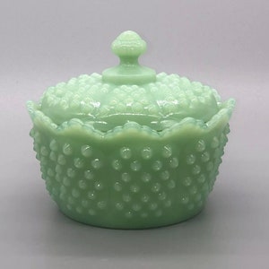May include: A vintage green glass candy dish with a lid. The dish has a scalloped edge and is covered in small raised dots.