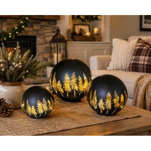 May include: Three spherical black lamps with a gold-toned forest silhouette design. Each globe features internal illumination that highlights the tree patterns against the dark surface, creating a glowing effect across the three different sizes.