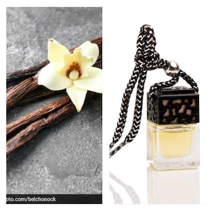 May include: A black and white car air freshener with a black string hanging from it. The air freshener is filled with a clear liquid and has a black decorative top. The air freshener is sitting on a white surface. The image also shows vanilla beans and a vanilla flower.