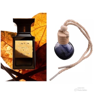 May include: A dark brown glass bottle with a gold label and a black cap. The bottle is sitting on a brown leaf. A small glass bottle with a blue liquid and a wooden cap is hanging from a rope. The bottle is a car air freshener.