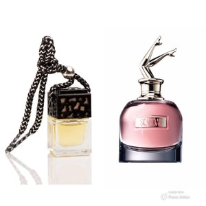 May include: Two perfume bottles against a white backdrop. One is a small, clear, square bottle with a black and white braided cord. The other is a pink perfume bottle with a silver cap shaped like legs.