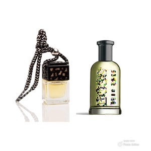 May include: A black and clear glass car air freshener with a black string hanging from it. The air freshener is filled with a yellow liquid. Next to it is a clear glass bottle with a black cap filled with a yellow liquid. The bottle has black text on it.
