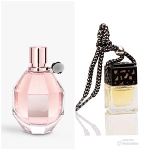 May include: Two perfume bottles, one pink and one clear, with black caps. The pink bottle is a larger, rounder shape with a geometric design. The clear bottle is smaller and rectangular with a black and gold cap. Both bottles are on a white background.
