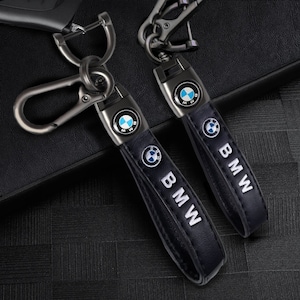 May include: Two black leather keyrings with silver metal clasps and a silver BMW logo. The keyrings have the word "BMW" written in white on the leather.