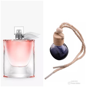 May include: A clear glass bottle of perfume with a pink liquid and a silver cap. The bottle is sitting on a white background. Next to it is a small, round, blue glass bottle with a wooden cap and a brown string.